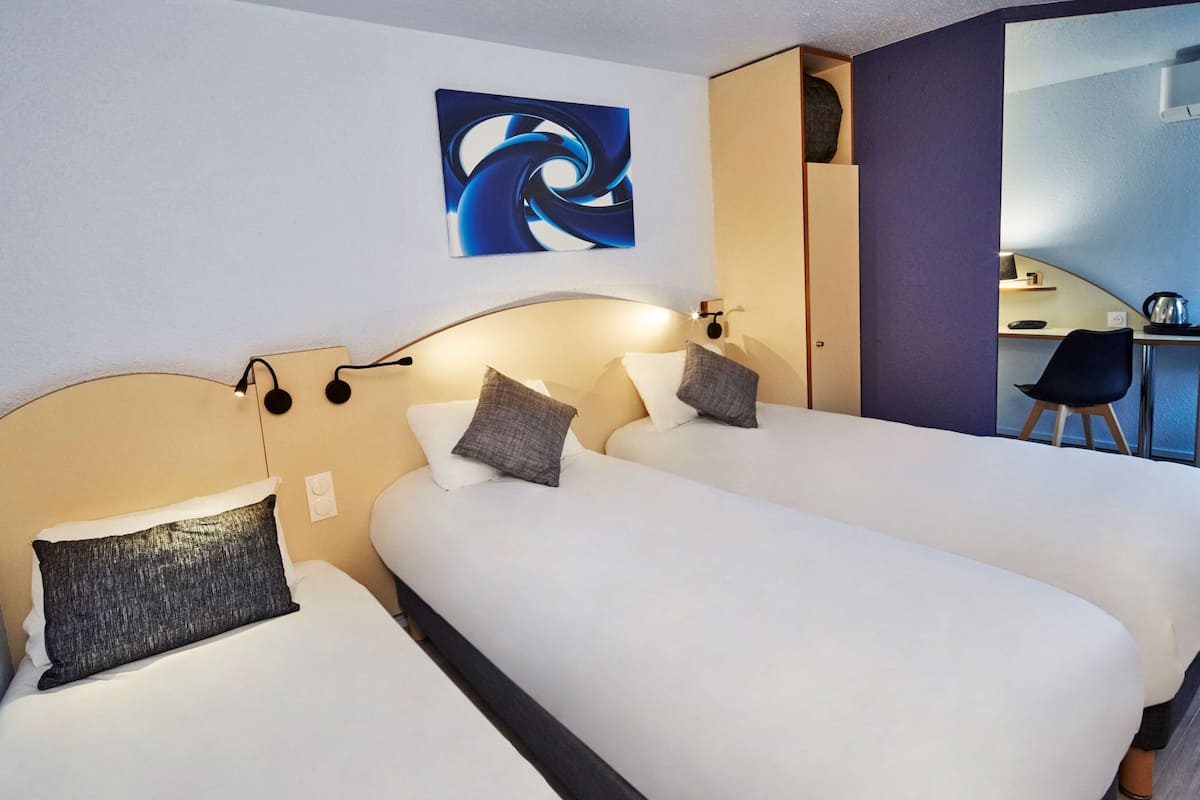 Quarto de hotel com duas camas, uma escrivaninha e uma cadeira.