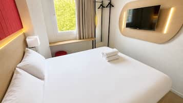Una habitación de hotel con una cama, un televisor montado en la pared, una ventana con cortinas y una pared decorada en rojo.
