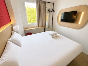Een hotelkamer met een bed, een aan de muur bevestigde televisie, een raam met gordijnen en een rode accentmuur.