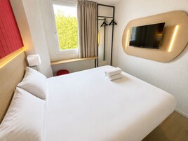 Una habitación de hotel con una cama, un televisor montado en la pared, una ventana con cortinas y una pared decorada en rojo.