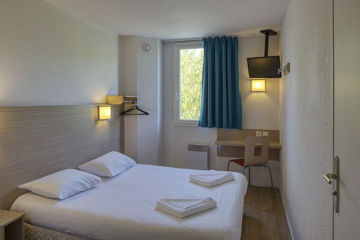 Een hotelkamer met een bed, nachtkastje en een bureau met stoel.