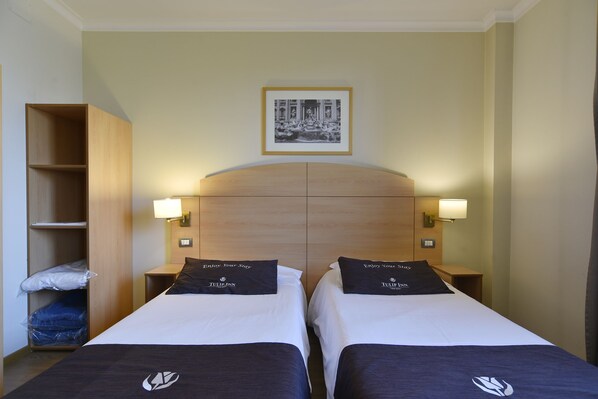A hotel room with two beds, a wooden headboard, a framed picture on the wall, and a trash bin.