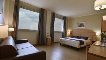 Een hotelkamer met een bed, een sofa, een bureau en een raam met gordijnen.