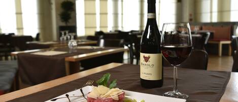 Une table à manger avec une assiette de nourriture, une bouteille de vin et un verre de vin rouge.
