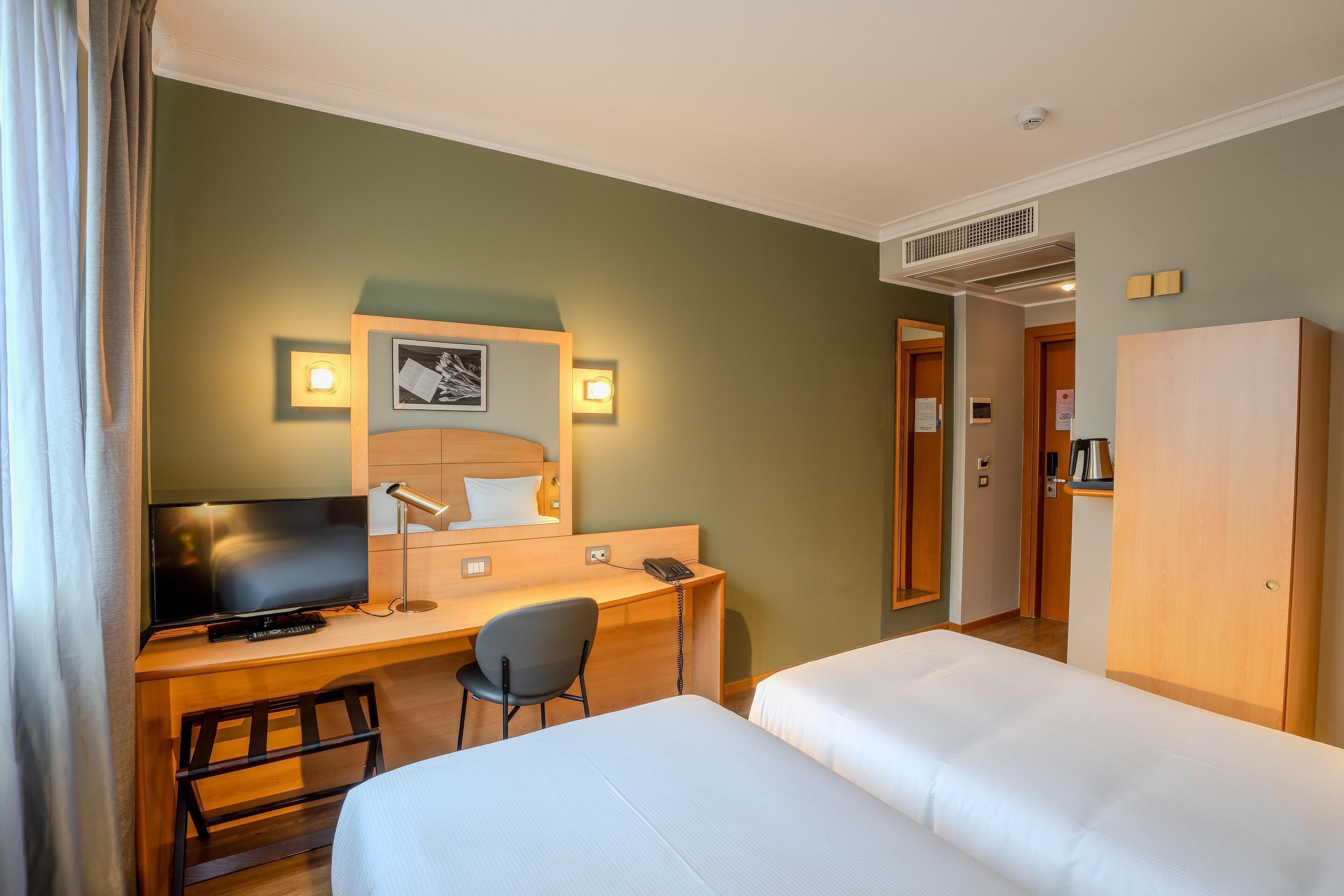 A hotel room with a bed, a desk with a chair, a television, and a mirror.