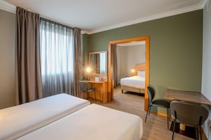 Quarto de hotel com duas camas, uma escrivaninha, uma cadeira e um espelho.