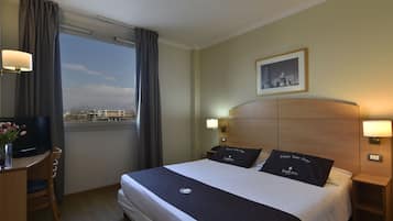 Une chambre d’hôtel avec un lit, un bureau, une télévision et une fenêtre avec des rideaux.