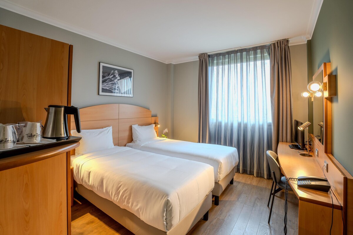 A hotel room with two beds, a desk with a telephone, a coffee maker, and a lamp.