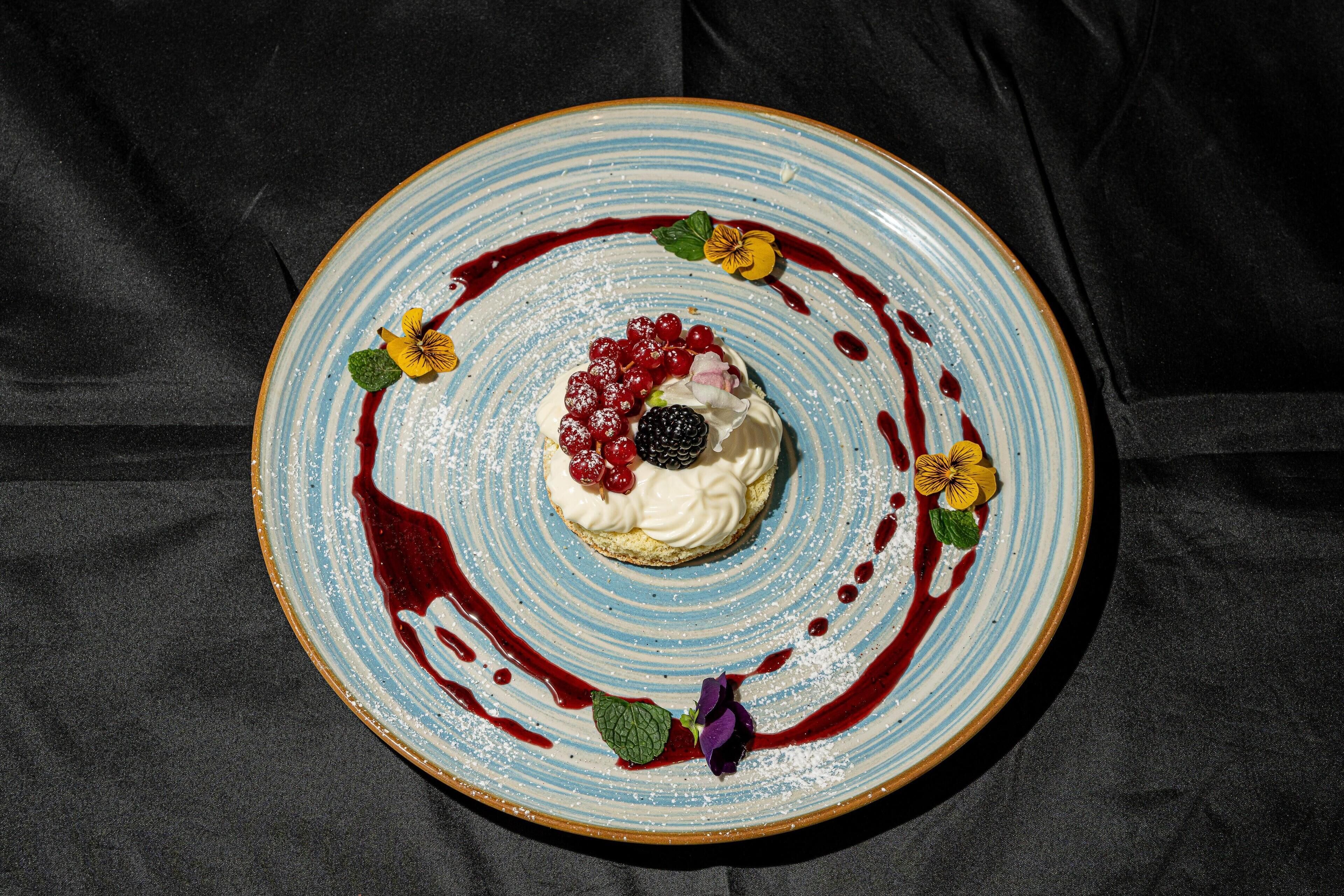 Postre a un plat amb un dibuix blau i blanc, envoltat de baies i fulles.
