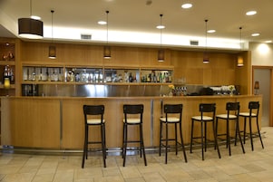 Uma área de bar com balcões de madeira, diversas prateleiras cheias de garrafas e seis banquetas.