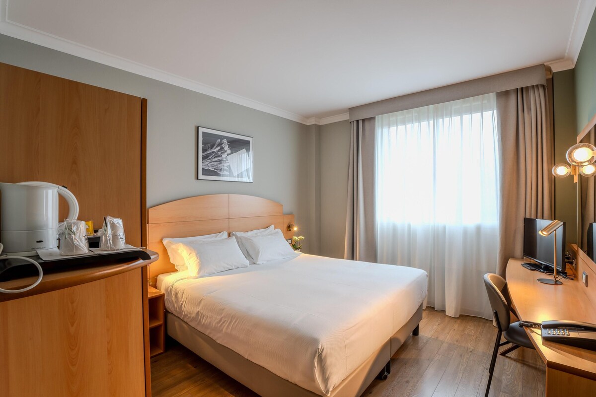 A hotel room with a bed, a desk with a computer, a coffee maker, and a TV.