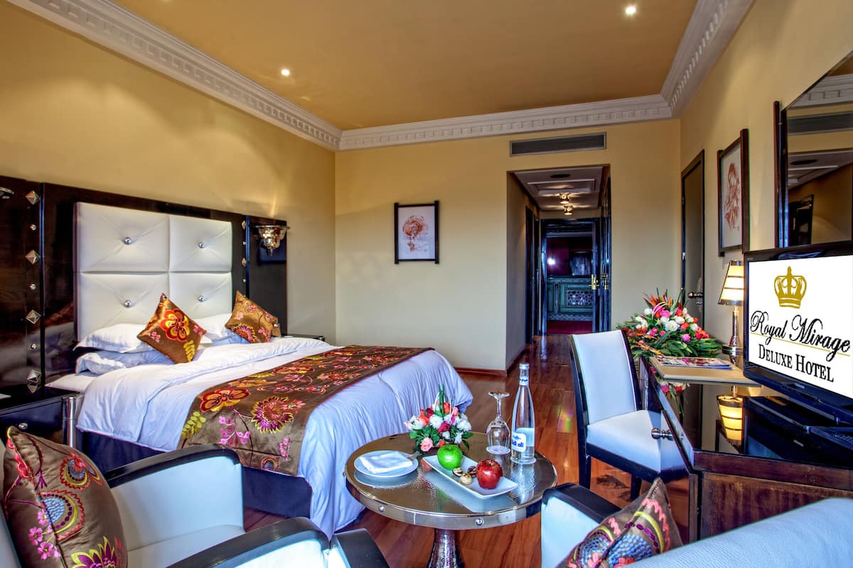 A hotel room with a large bed, a sitting area with a table, and a TV.
