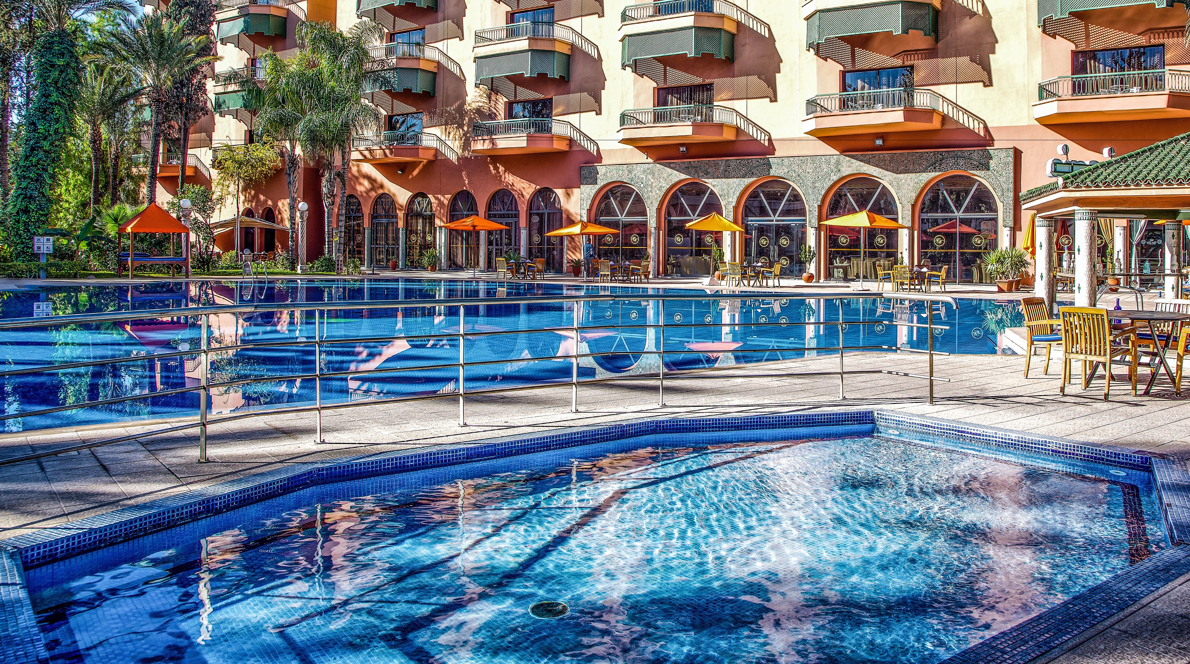 A hotel pool area with multiple swimming pools, sun loungers, and outdoor seating.