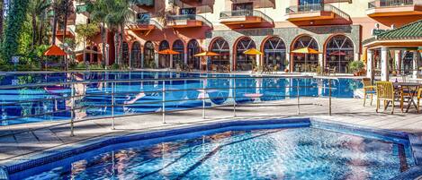 A hotel pool area with multiple swimming pools, sun loungers, and outdoor seating.