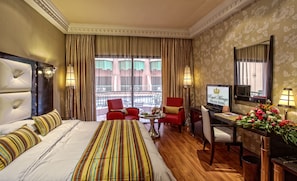 Quarto de hotel com uma cama grande, uma mesa com televisão, uma cadeira e vista para a varanda.