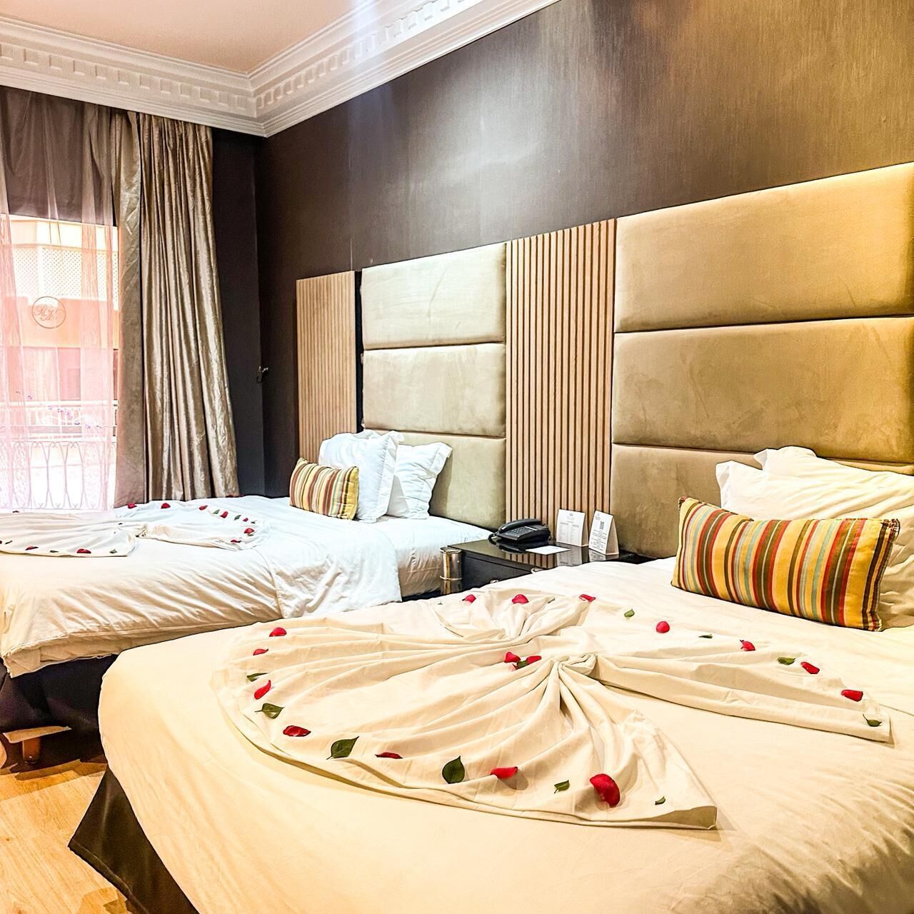 A hotel room with two beds, a large padded headboard, and a bedside table with a phone and papers.