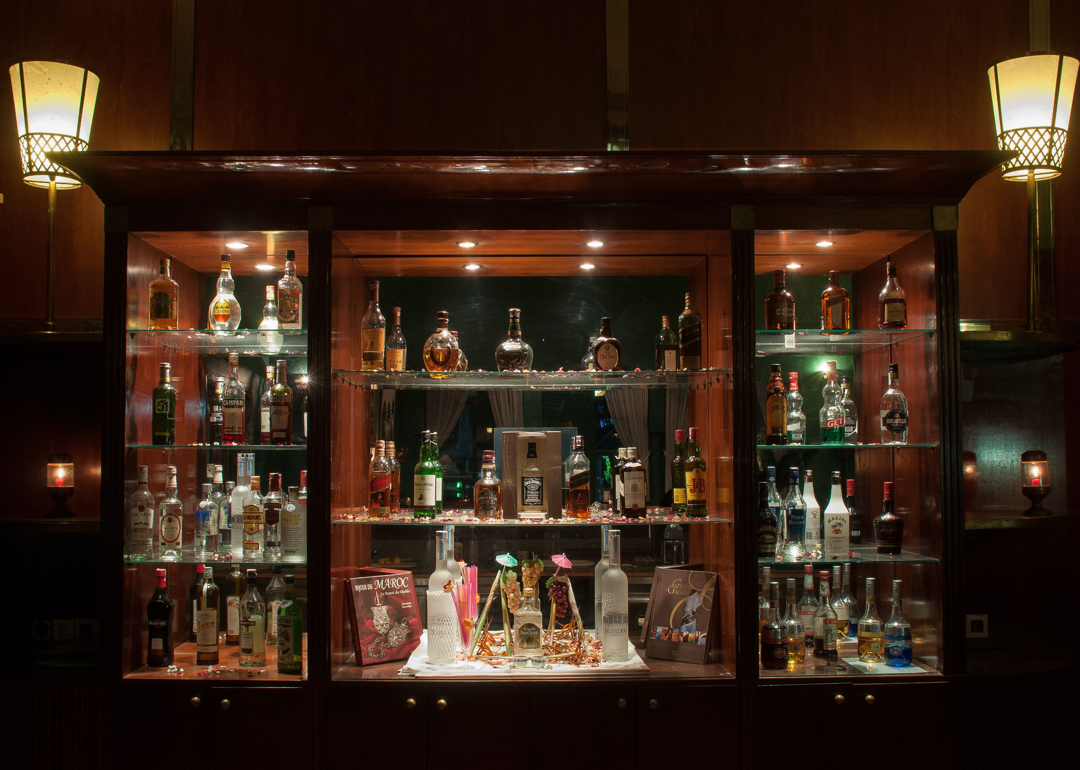 Un bar con numerosas estanterías llenas de botellas de licores, una exhibición de copas y una botella de Bordeau.