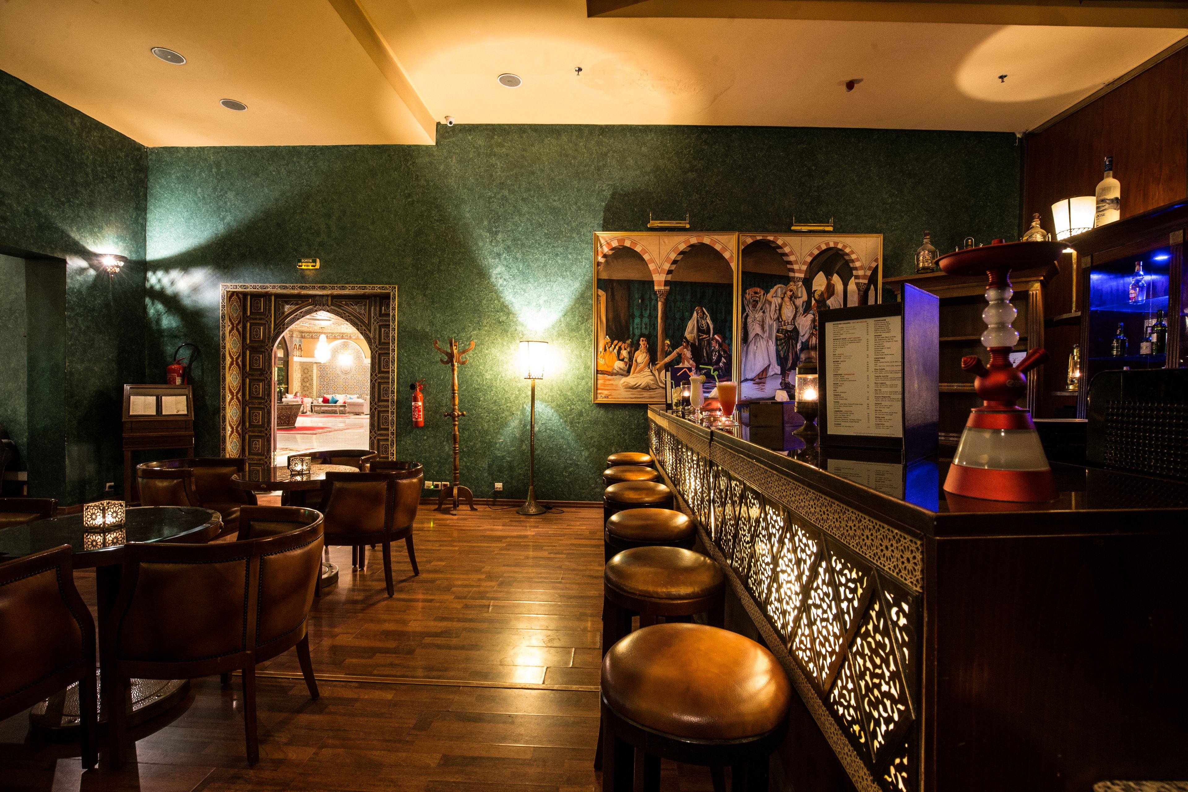 A bar area with wooden flooring, leather bar stools, and a decorative wall with a framed picture.