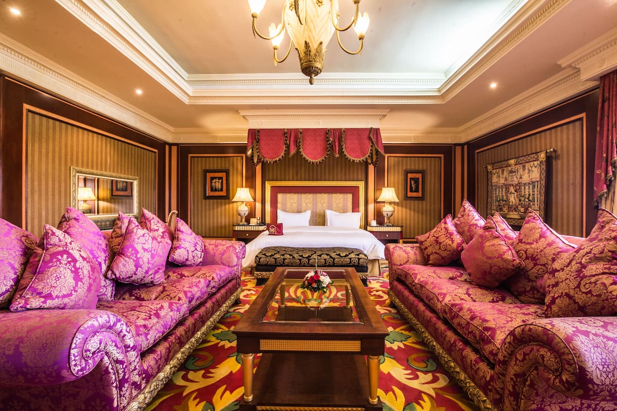 A luxurious hotel room with a large bed, two sofas, a coffee table, and a chandelier.