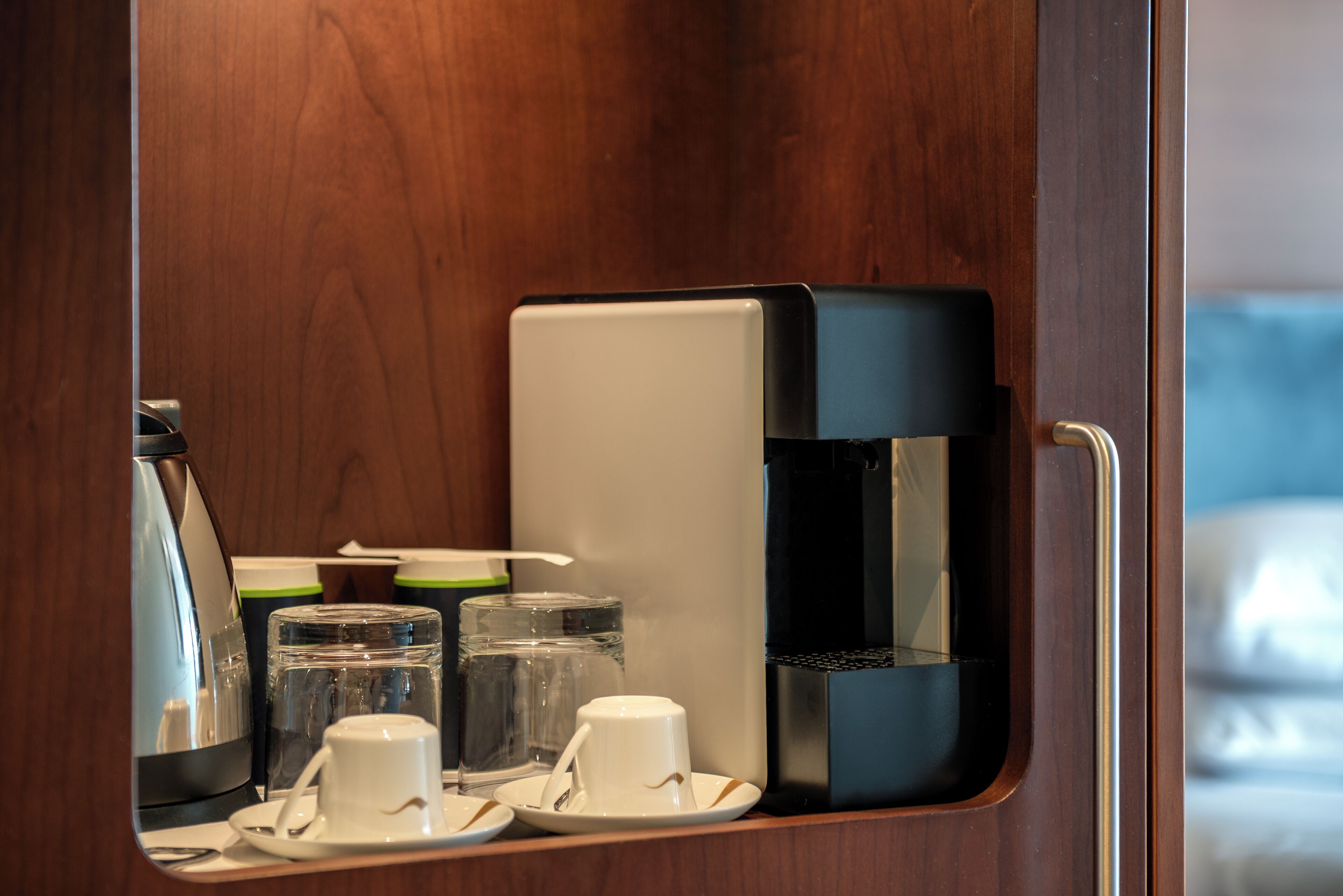 A compact kitchenette with a coffee maker, a water dispenser, and a glass of water on a tray.