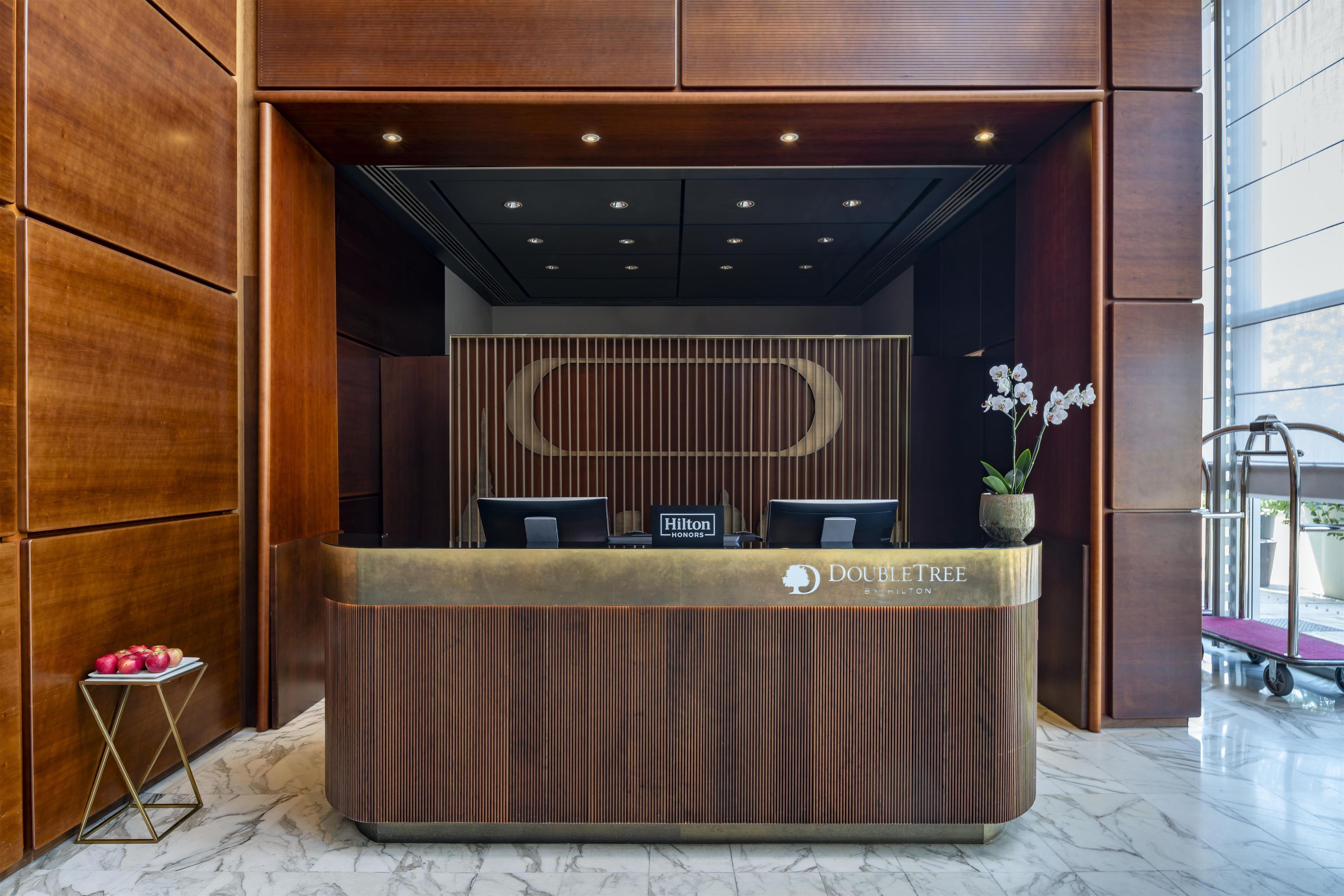 Ein Empfangsschalter mit Holzoptik, zwei Stühle, eine Topf-Orchidee und ein Schild mit der Aufschrift 'Hilton Honors'.