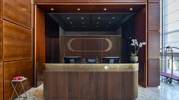 Ein Empfangsschalter mit Holzoptik, zwei Stühle, eine Topf-Orchidee und ein Schild mit der Aufschrift 'Hilton Honors'.