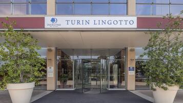 Der Eingang eines Hotels mit einer Drehtür und je einer Pflanzengruppe auf beiden Seiten.