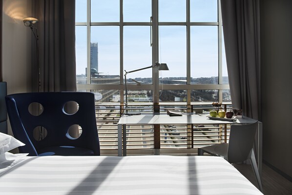 A hotel room with a large window, a bed, a desk with a lamp, and a chair. - DoubleTree by Hilton Turin Lingotto (Turin)
