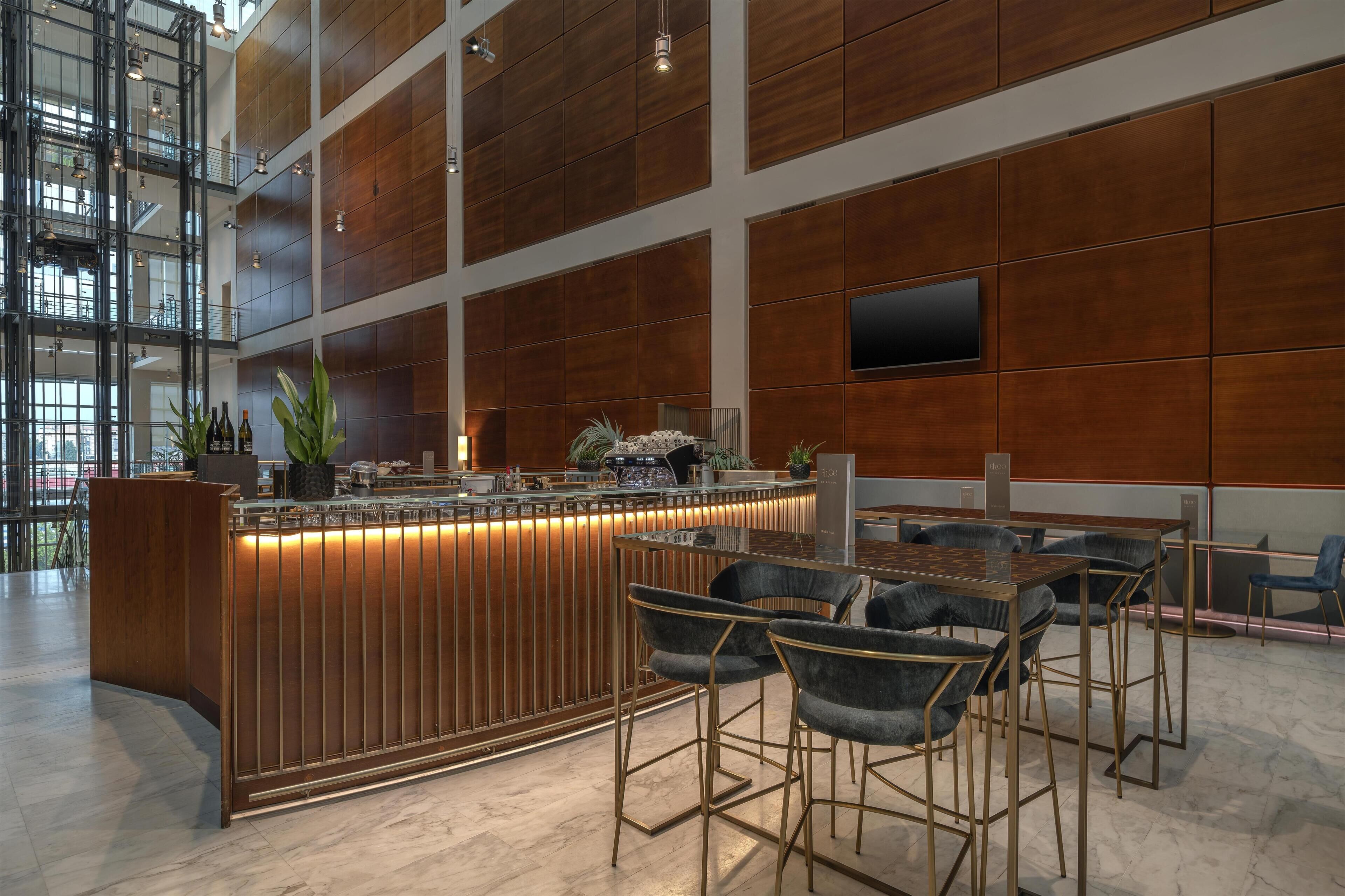 A modern bar area with a wooden panel wall, a counter with bar stools, and a large window providing natural light.