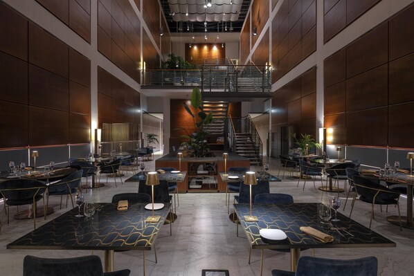 A spacious, modern hotel lobby with multiple dining areas, a central staircase, and a mezzanine level. - DoubleTree by Hilton Turin Lingotto (Turin)