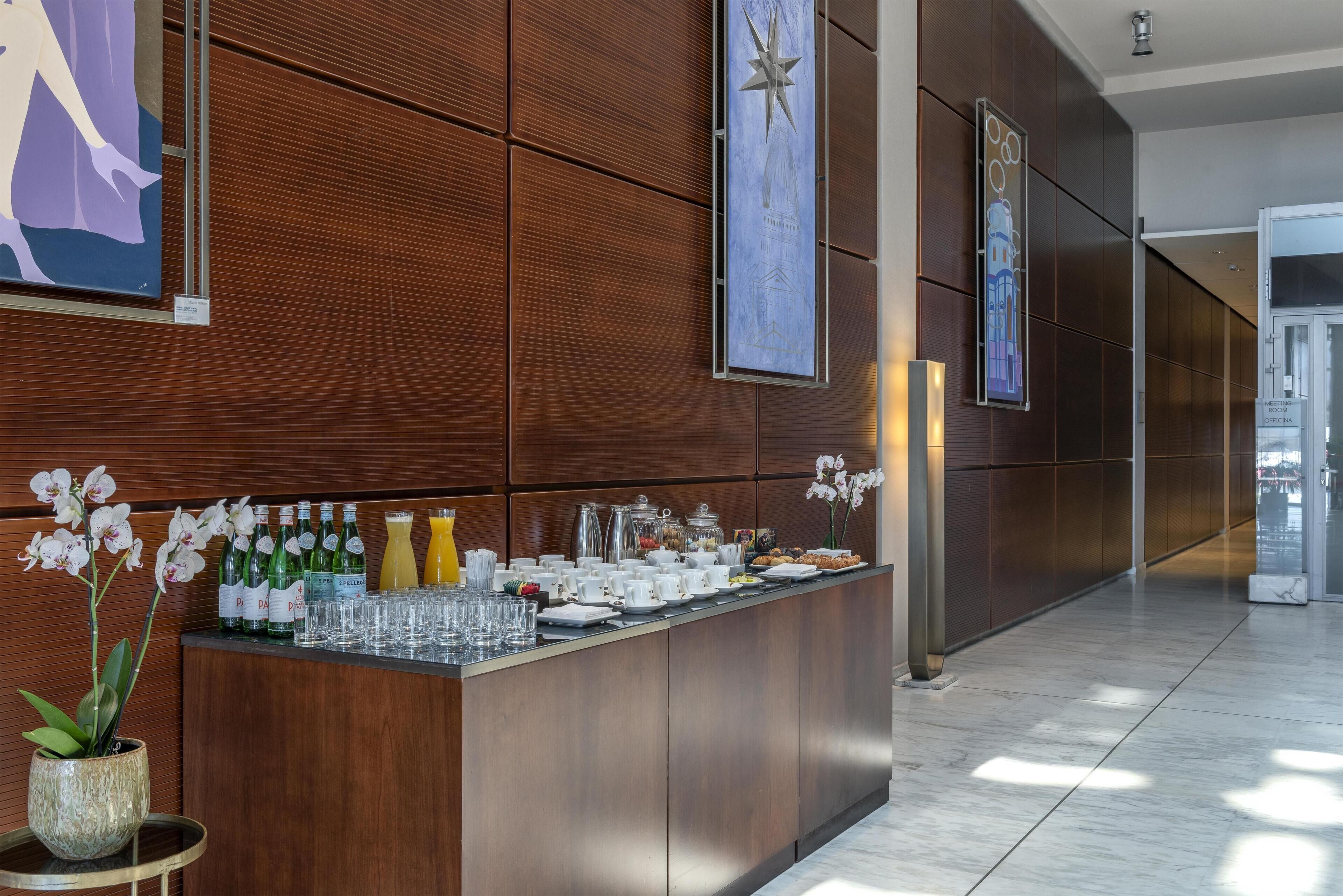 A reception area with a wooden panel wall, a counter with beverages and cups, and a sign indicating a meeting room.
