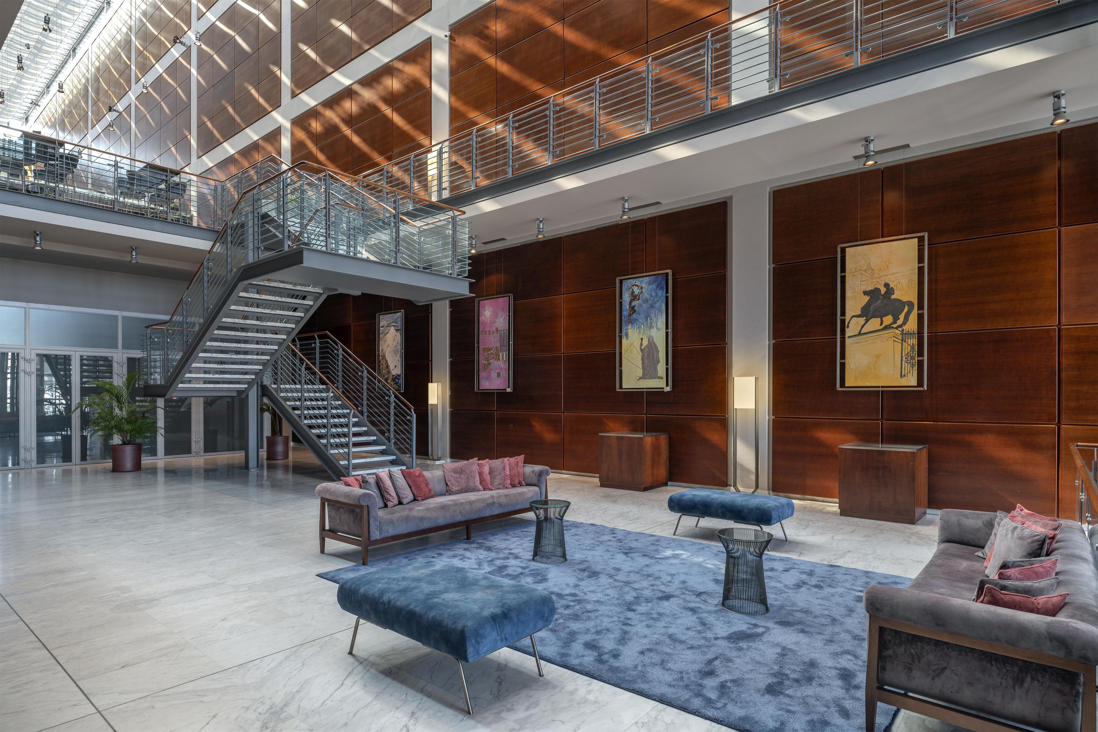 A spacious lobby with a high ceiling, a staircase, and a seating area with sofas and a coffee table.