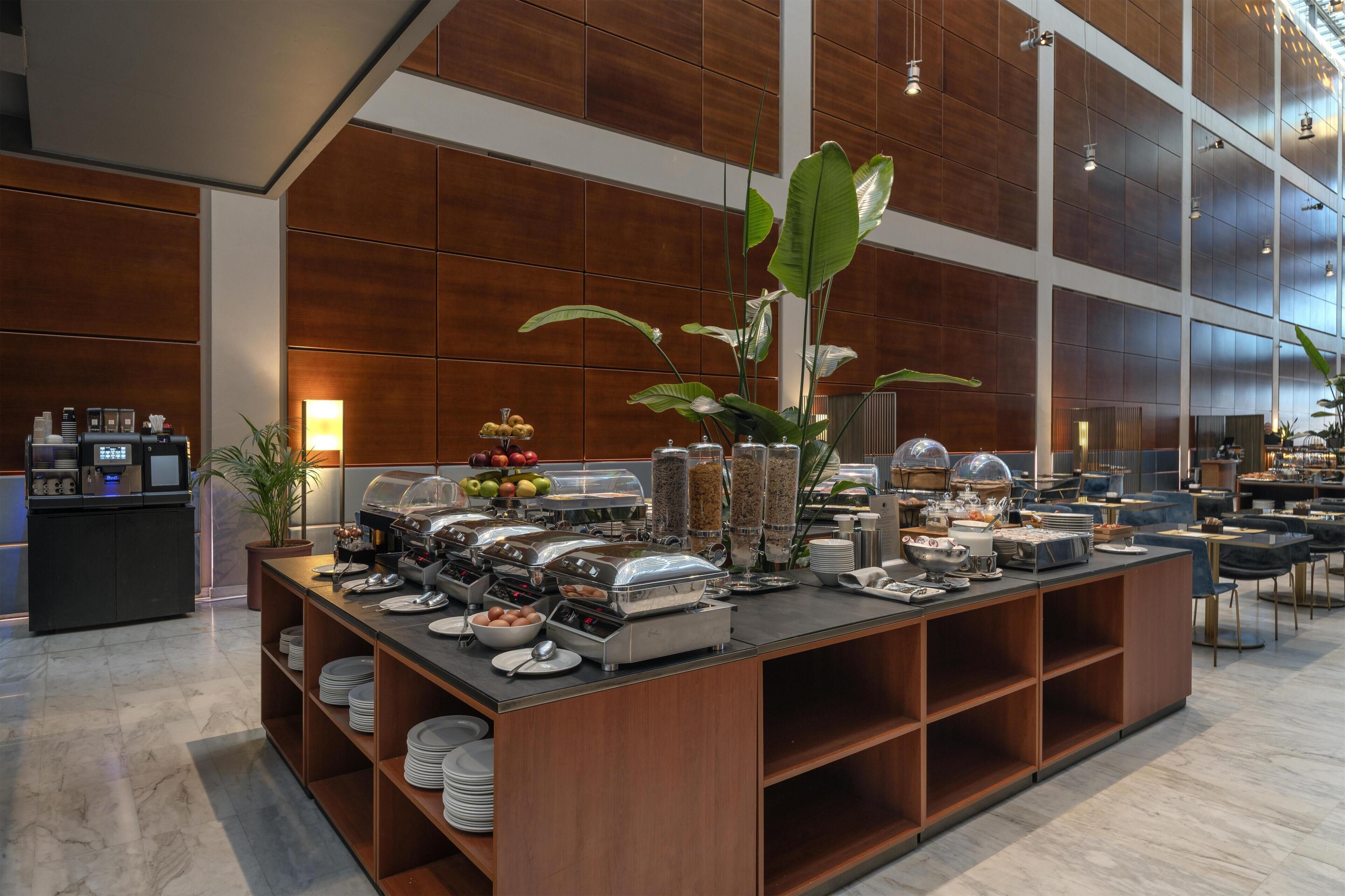 A buffet setup with various food items and a coffee station in a modern hotel setting.