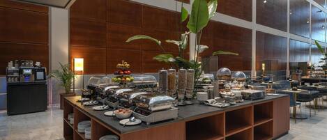 A buffet setup with various food items and a coffee station in a modern hotel setting.