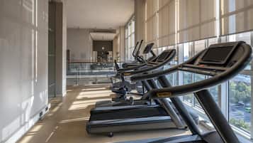 A gym with treadmills aligned along a wall with large windows.