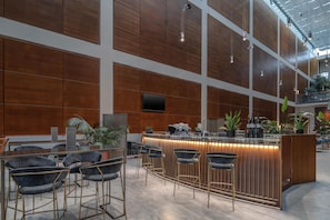 A modern bar area with a wooden counter, bar stools, and a flat-screen TV mounted on the wall. - DoubleTree by Hilton Turin Lingotto (Turin)