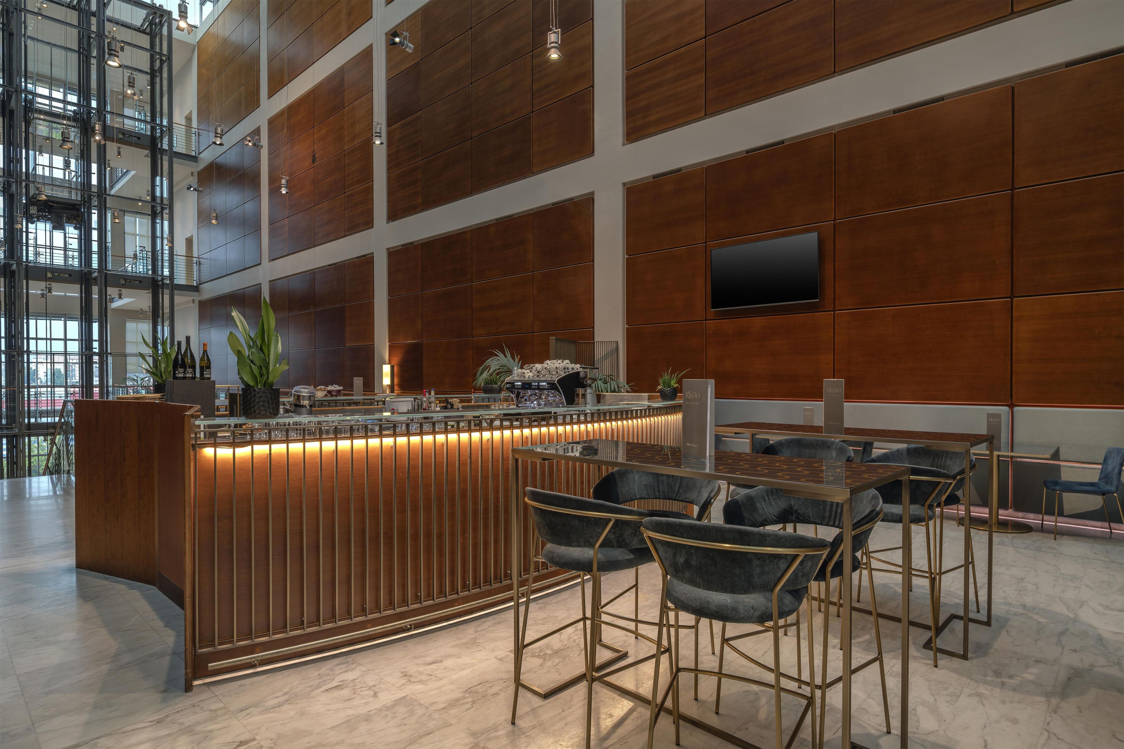 Zona de bar moderna con pared de paneles de madera, una barra con taburetes y un amplio ventanal que proporciona luz natural.