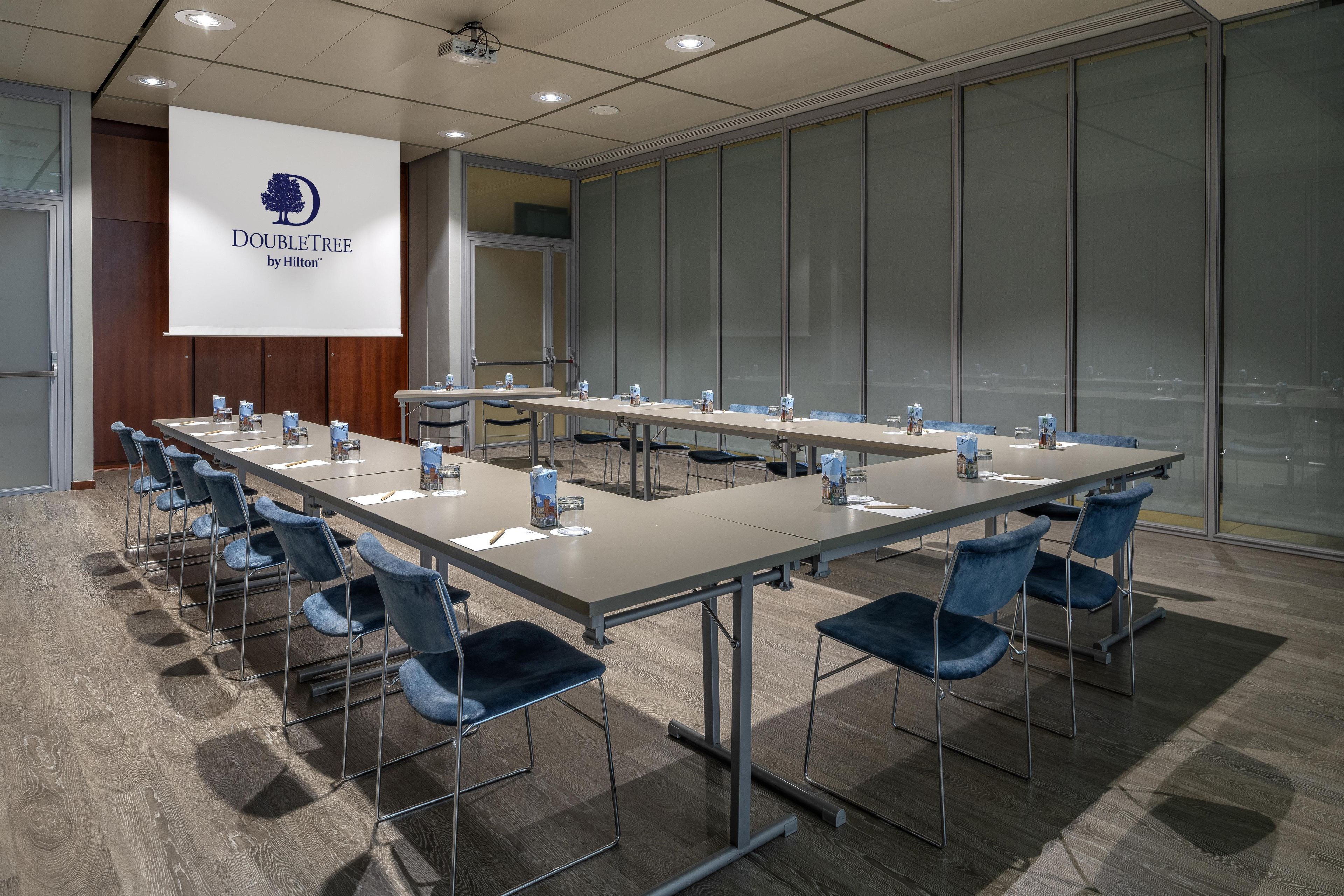 Un salón de conferencias con una larga mesa, sillas, una pantalla de proyector y un ventanal.