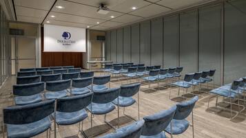 Ein Konferenzraum mit Stuhlreihen, einem Rednerpult und einer Präsentationsleinwand.