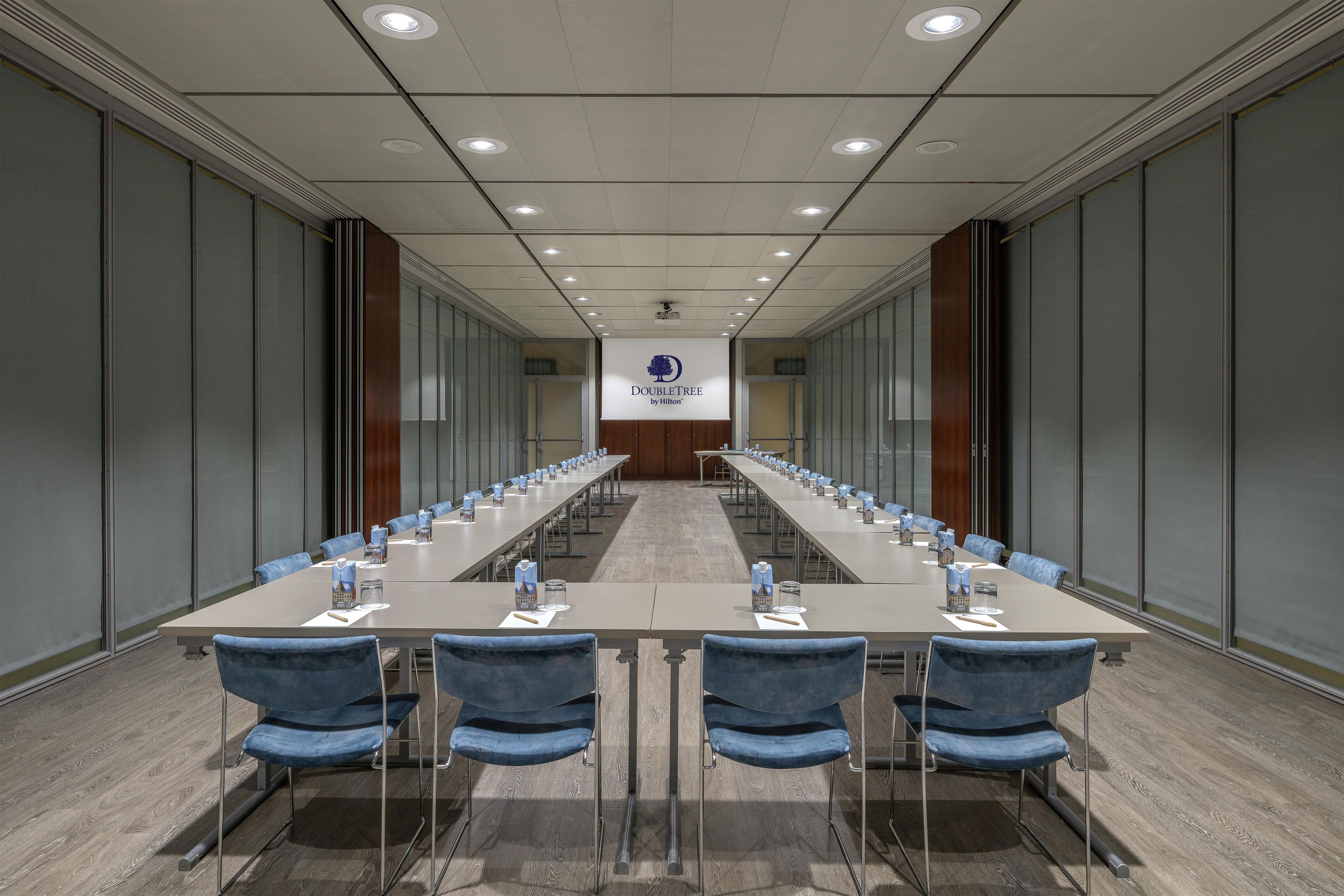 Un salón de conferencias con una larga mesa, sillas azules y un logotipo en la pared.