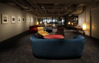 A modern lounge area with a blue sofa, yellow and red chairs, and a red bean bag.