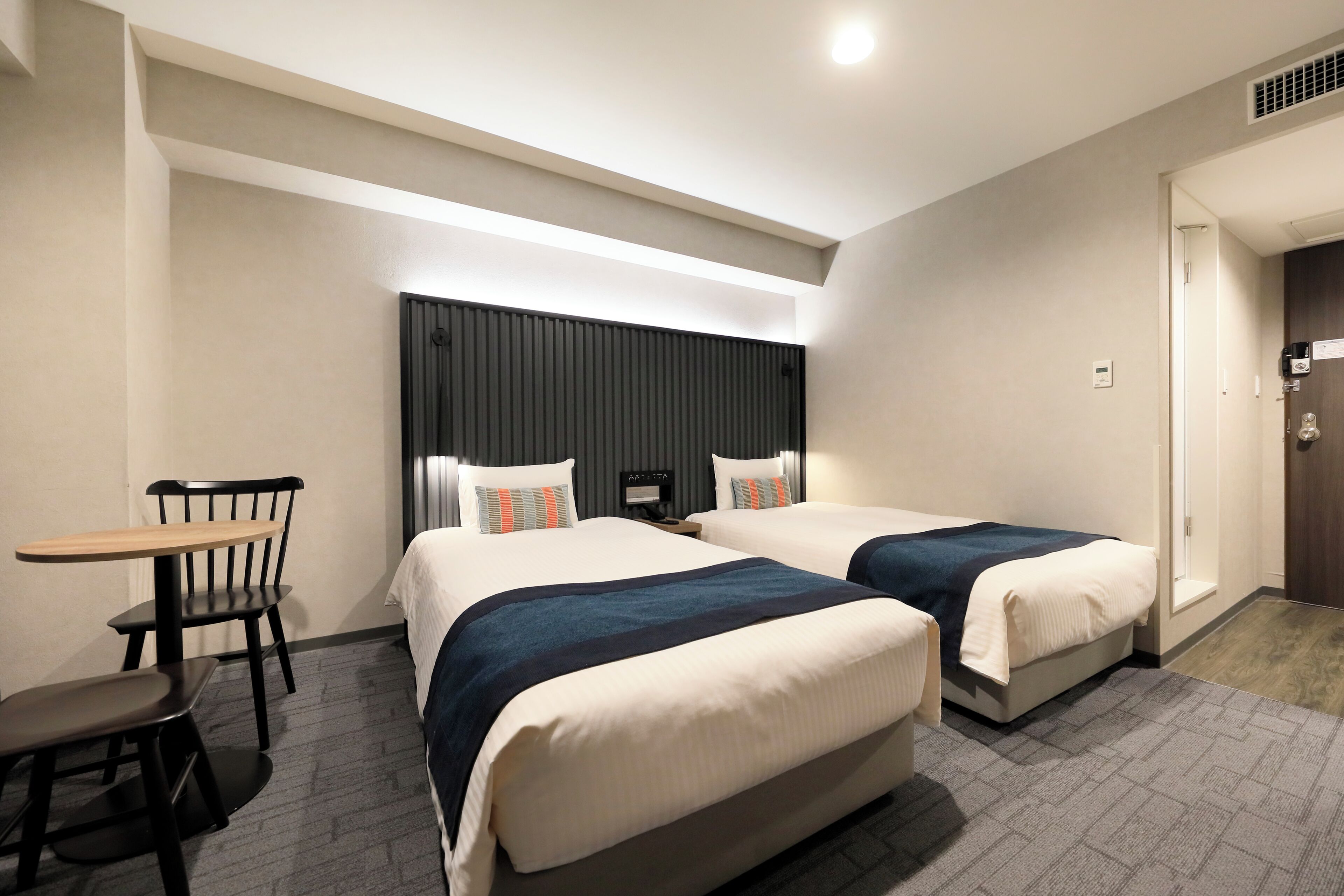 A hotel room with two beds, a desk, and a chair.