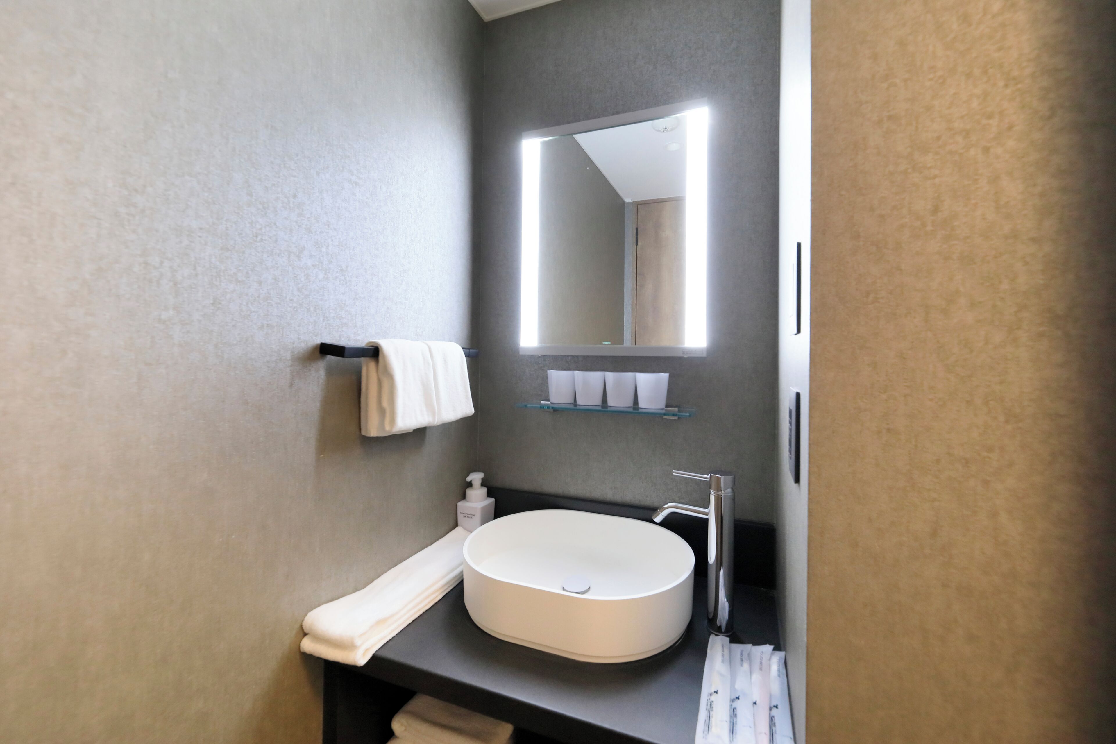 A modern bathroom with a large mirror, a round sink, and a towel rack.