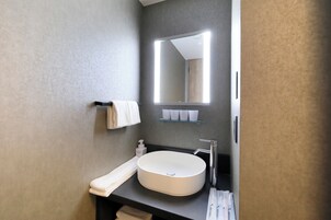 A modern bathroom with a large mirror, a round sink, and a towel rack.