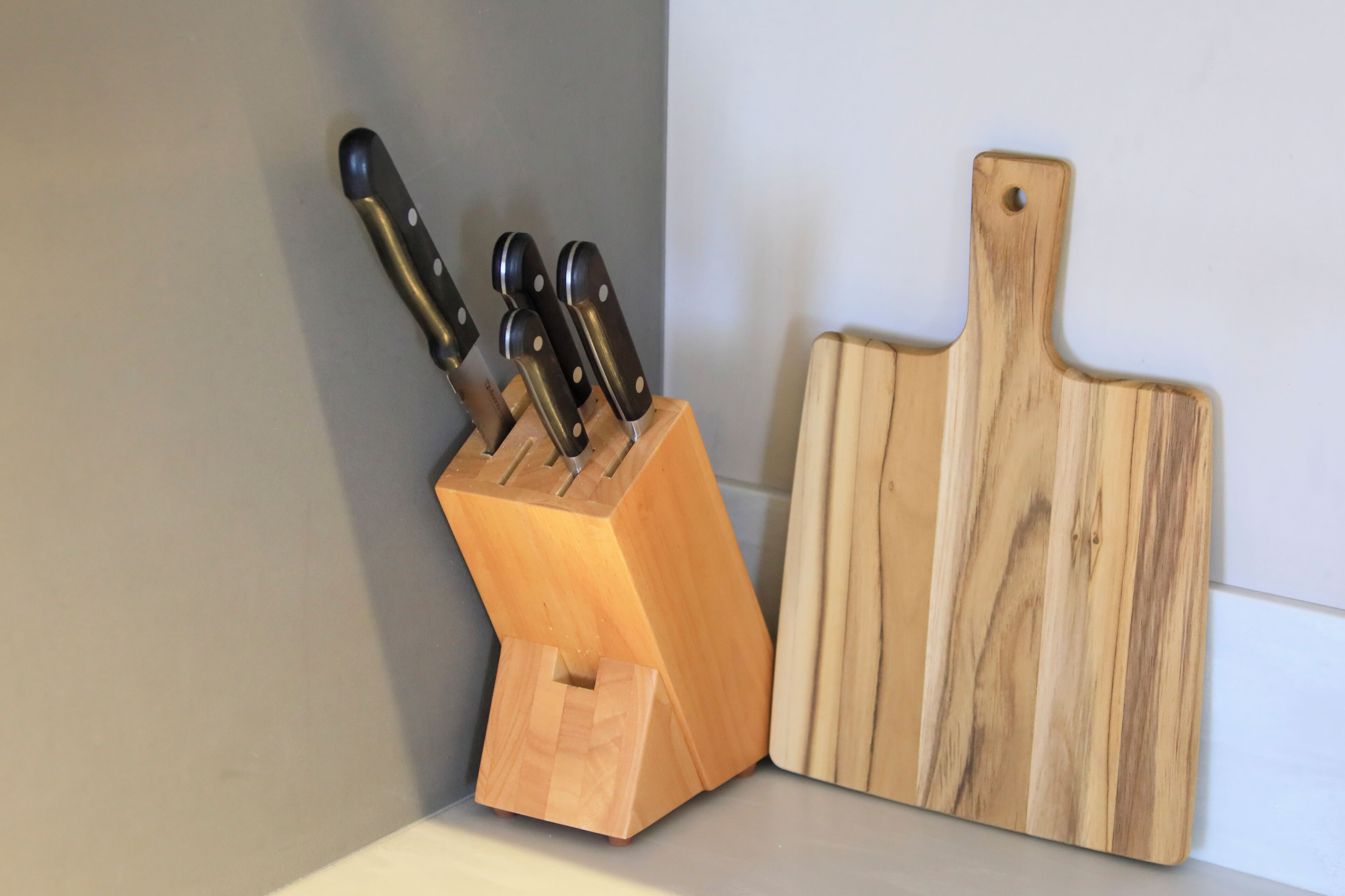 A wooden knife block with knives and a wooden cutting board on a countertop.