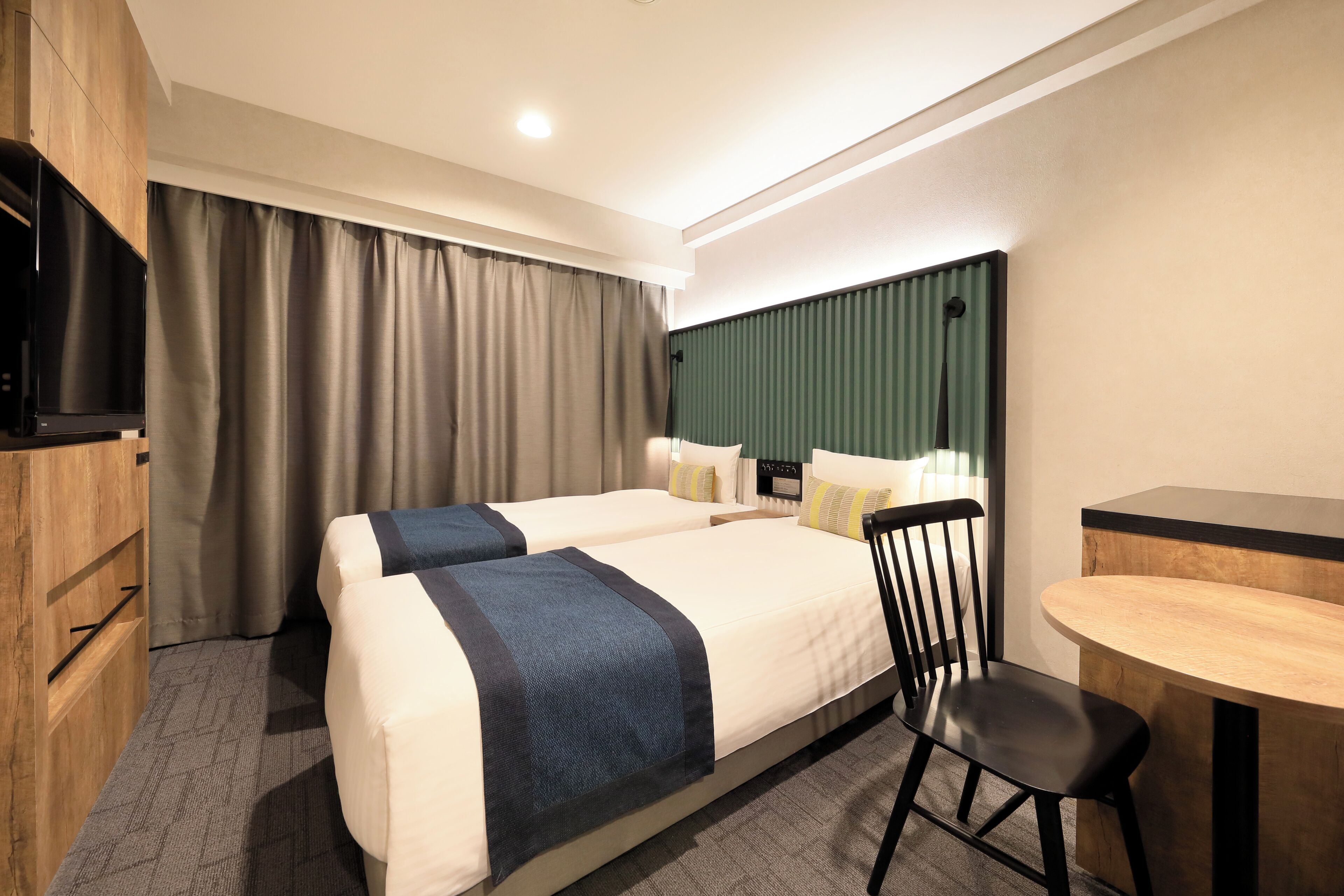 A hotel room with two beds, a desk, a chair, a television, and a large window with curtains.