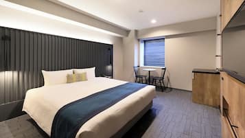 Een hotelkamer met een groot bed, een bureau, een stoel en een raam met jaloezieën.