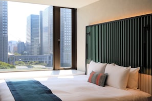 Habitación de hotel con una cama grande, vistas a edificios altos y una ventana con persianas.