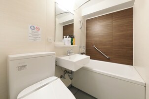 A bathroom with a toilet, sink, and bathtub. There is a mirror above the sink and a wooden door to the right.