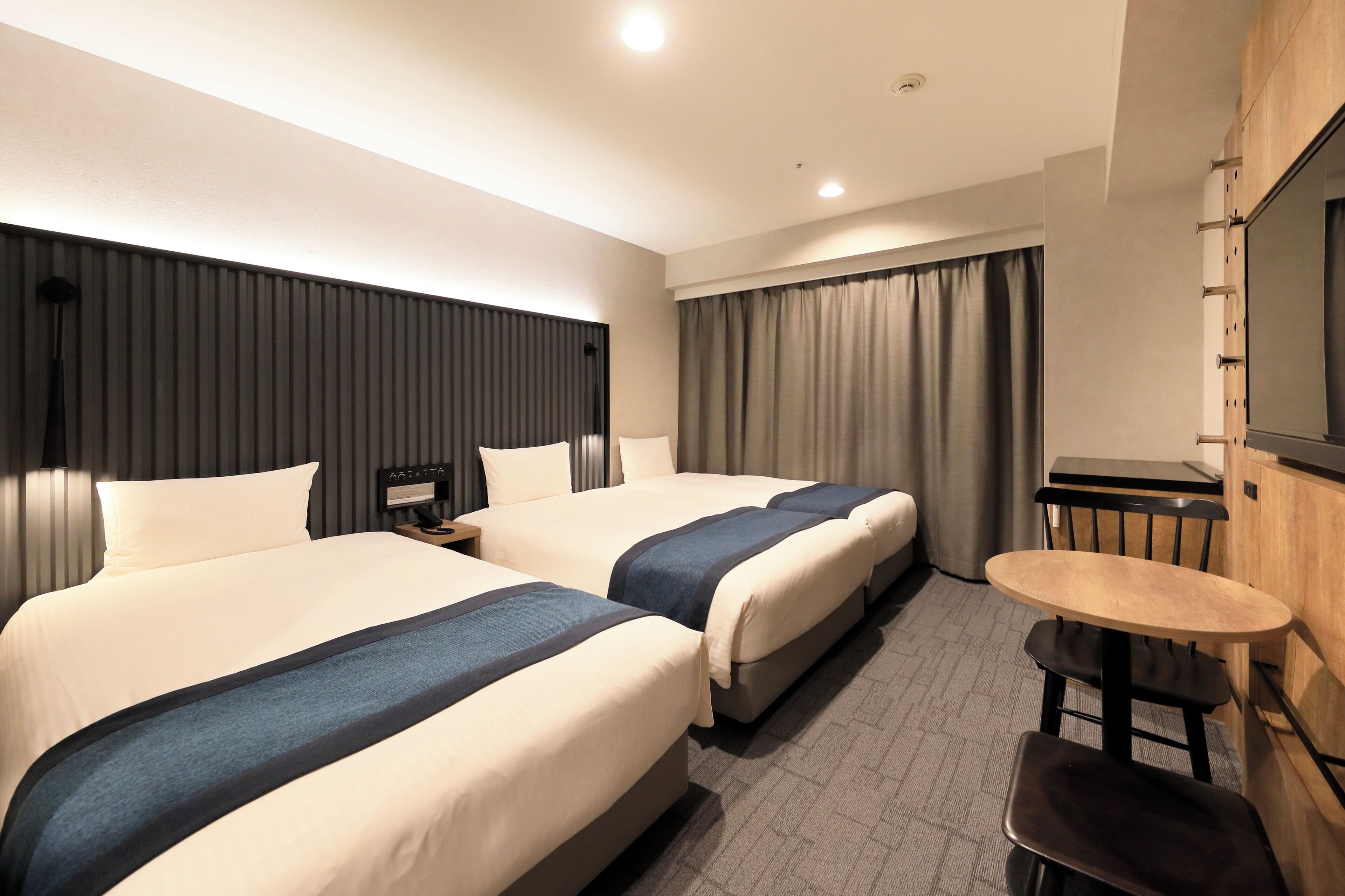 A hotel room with two beds, a desk, a chair, and a TV mounted on the wall.